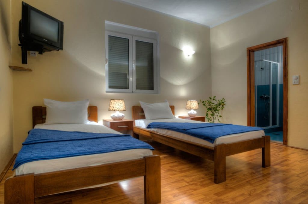 Bedroom with two beds, wooden furniture, and an en-suite bathroom in a hotel, Buljarica, Montenegro.