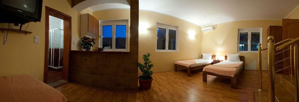 Bedroom interior in the Buljarica hotel, Montenegro: two beds, wooden floor, brick finish, and a view of the staircase.
