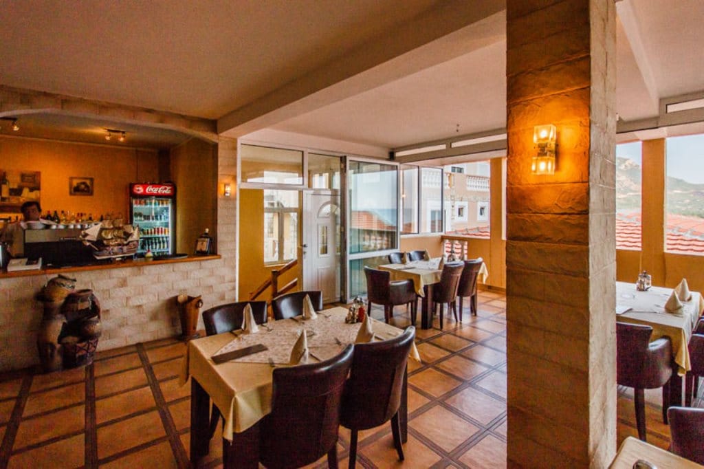 Hotel restaurant interior in Buljarica, Montenegro: stone finishes, dark furniture, and panoramic windows with mountain views.