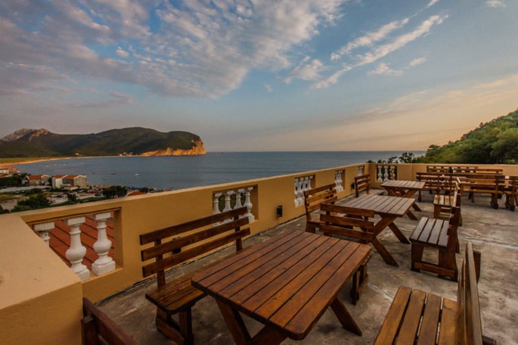 Open hotel terrace in Buljarica, Montenegro, with wooden tables and panoramic views of the sea and mountains.