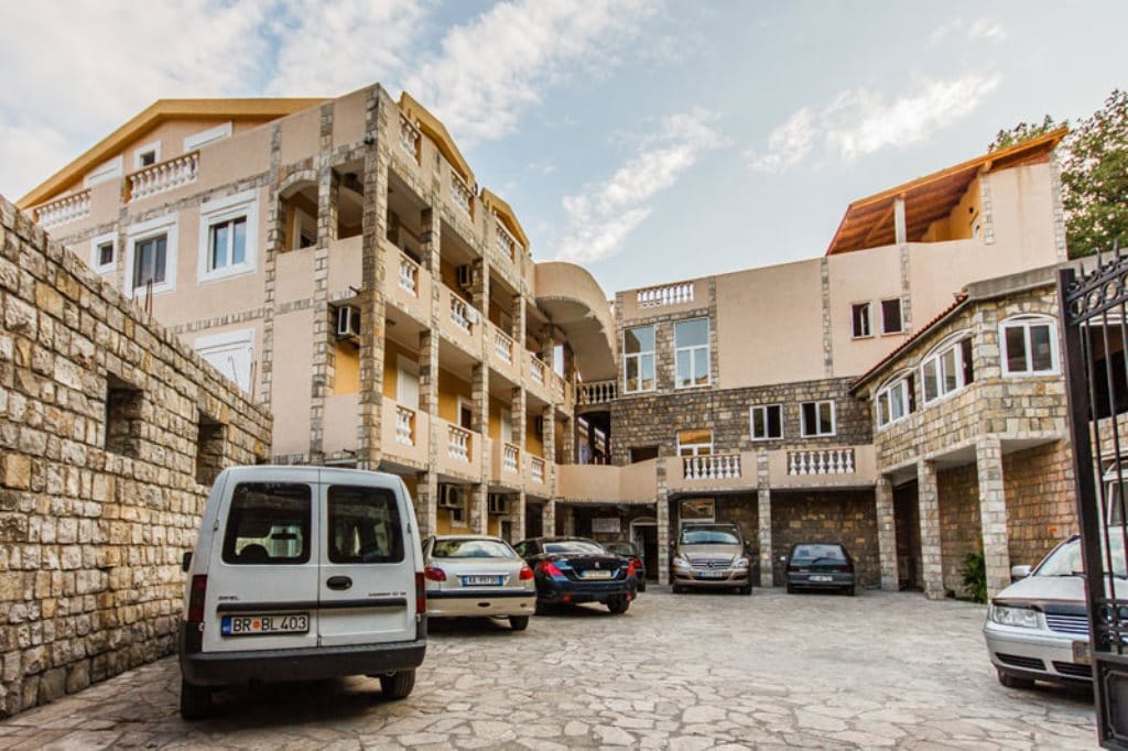 Hotel facade in Buljarica, Montenegro: a three-story stone building with parking in the inner courtyard and balconies.