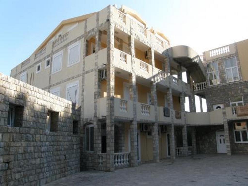 Three-story hotel in Buljarica, Montenegro: stone and beige stucco facade with open terraces and columns.