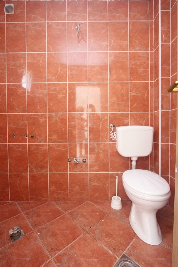 Bathroom in a house in Muo, Montenegro: red marble-effect tile finish, installed toilet, plumbing fixtures.