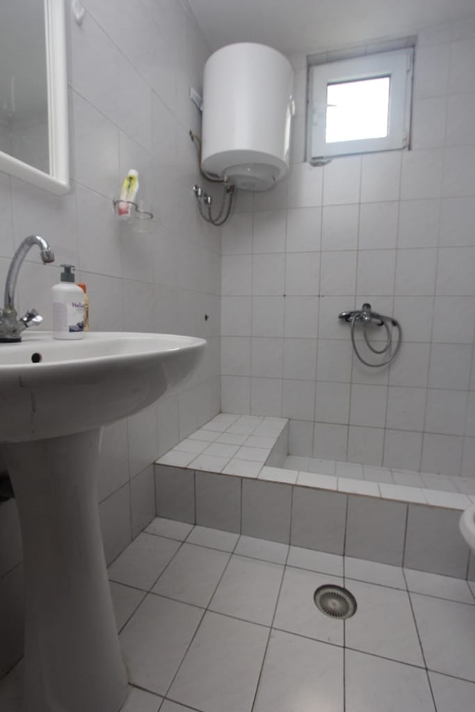 Bathroom in a house in Muo, Montenegro: white tiles, pedestal sink, shower area, and a water heater on the wall.