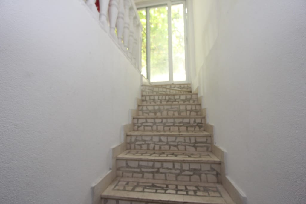 Staircase with stone finishes and white railings in a house in Muo, Montenegro, leading to a panoramic glass door.