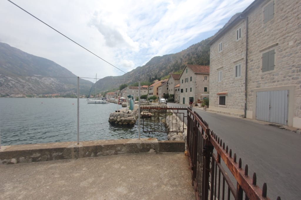 View of a stone house by the sea in Muo, Montenegro: waterfront promenade, yacht pier, and panoramic view of the Bay of Kotor.
