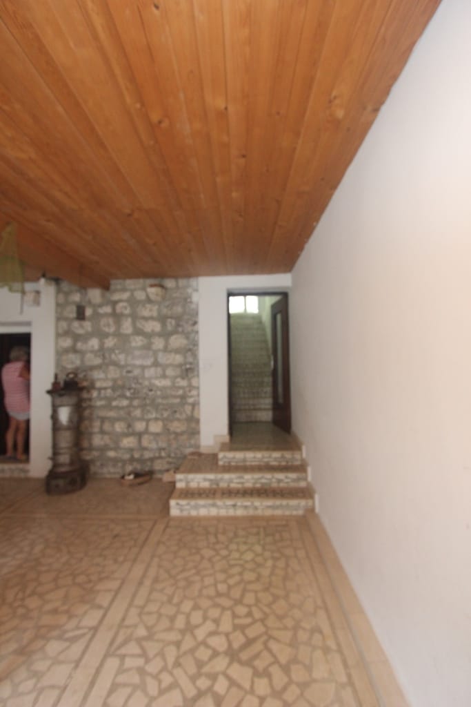 Living room in a house in Muo, Montenegro: stone wall, wooden ceiling, floor tiles, and staircase to the second floor.