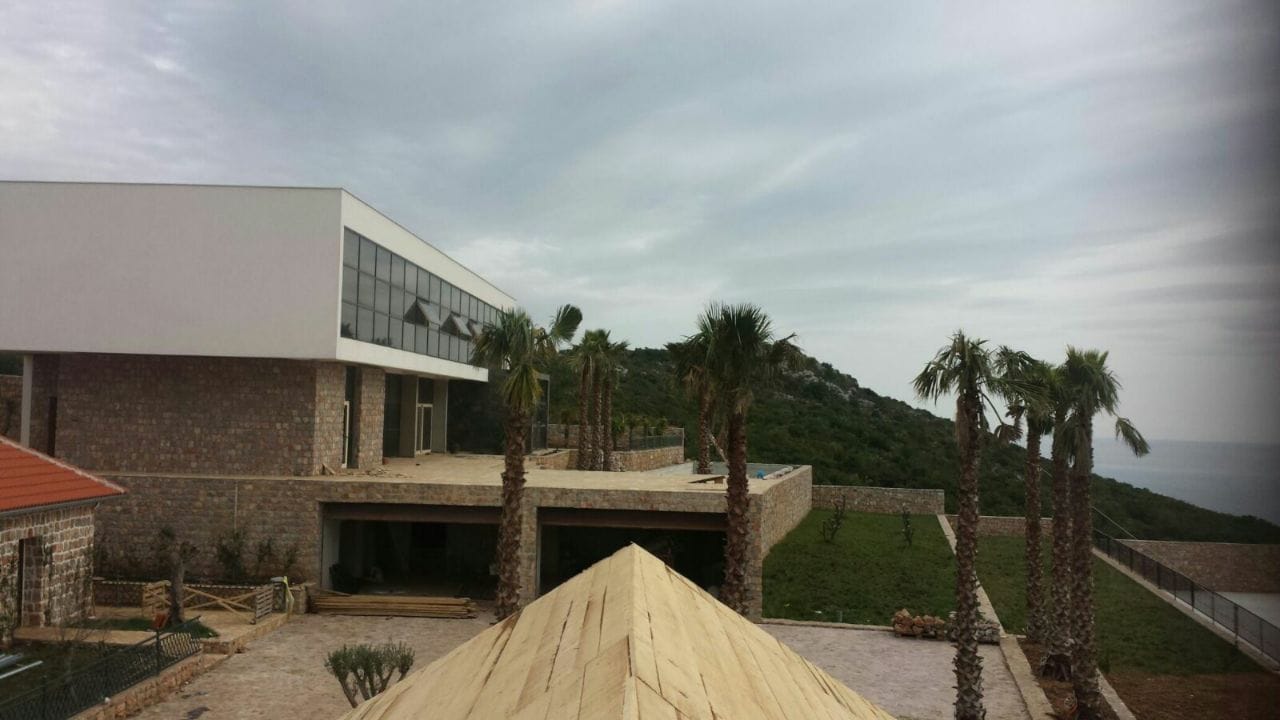 Modern villa in Krimovica, Montenegro: stone facade, panoramic windows, and palm trees against a seaside landscape.