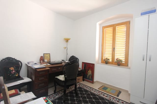 Office in a house in Muo, Montenegro: antique desk, black chairs, white cabinet, and a window with wooden shutters.