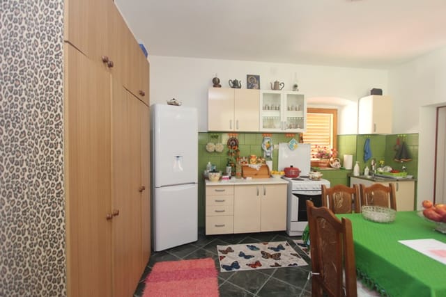 Kitchen in a house in Muo, Montenegro: light-colored cabinetry, green backsplash, dining area, and built-in wardrobe in the interior.