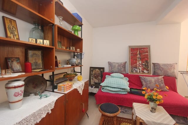 Cozy living room with a red sofa and a wooden shelving unit in a house for sale in Muo, Montenegro.