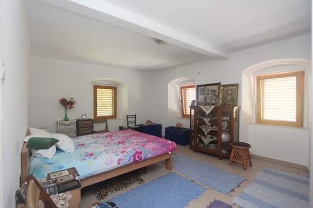 Bedroom in a house in Muo, Montenegro: double bed, vintage sideboard, light walls, and windows with wooden shutters.
