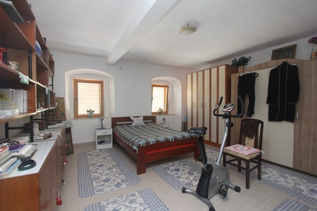 Bedroom in a house in Muo, Montenegro: double bed, wardrobes, exercise bike, light finishes, and arched windows.
