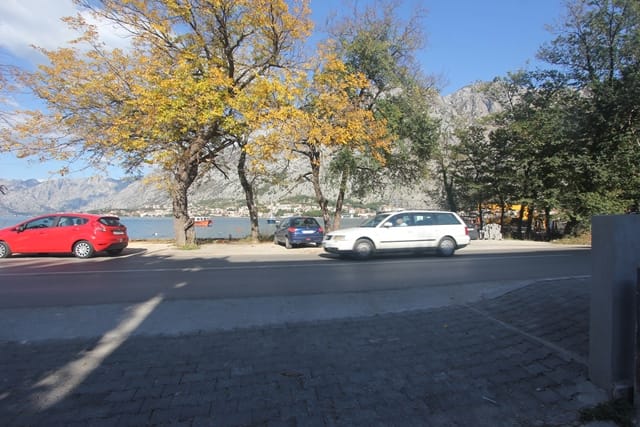 View of Kotor Bay and the mountains from a house in Muo, Montenegro: road, parked cars, and autumn trees.