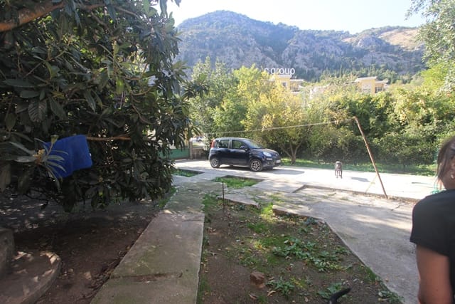 View of the residential area of the house in Muo, Montenegro: a green garden, car parking, and a mountain landscape in the background.