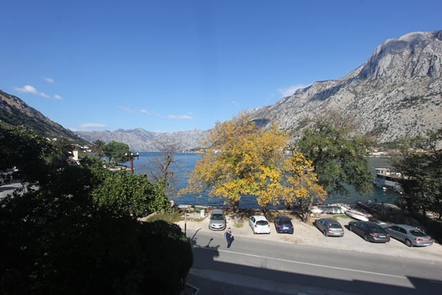 Panoramic view of the Bay of Kotor and mountains from a house in Muo, Montenegro, with a coastal road and parking.