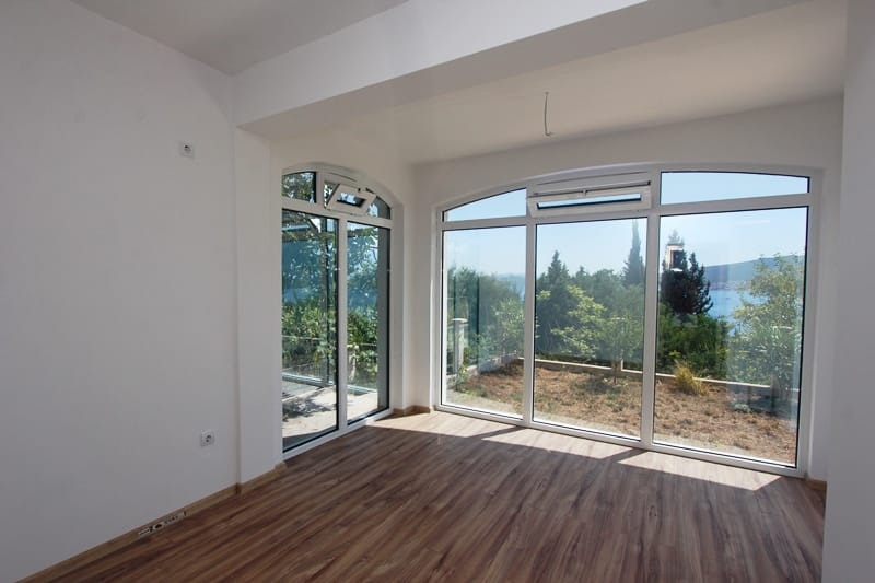 Bright living room with panoramic windows and sea view in a house, Baošići, Montenegro. Laminate flooring and white walls.
