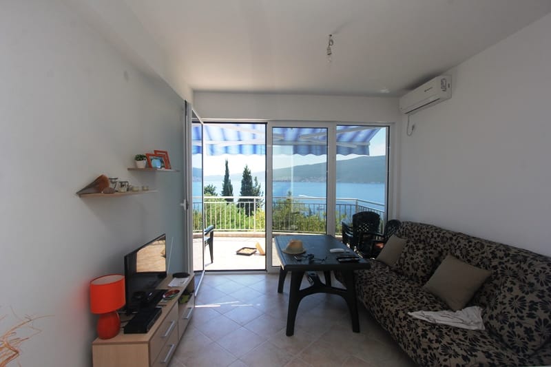 Living room with access to the terrace and sea view in a house, Baošići, Montenegro: sofa, TV area, and panoramic glazing.