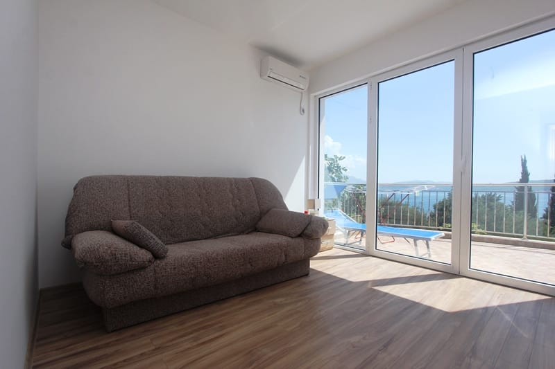 Living room in a house in Baošići, Montenegro: sofa, panoramic windows with sea view, and access to a terrace with a sun lounger.