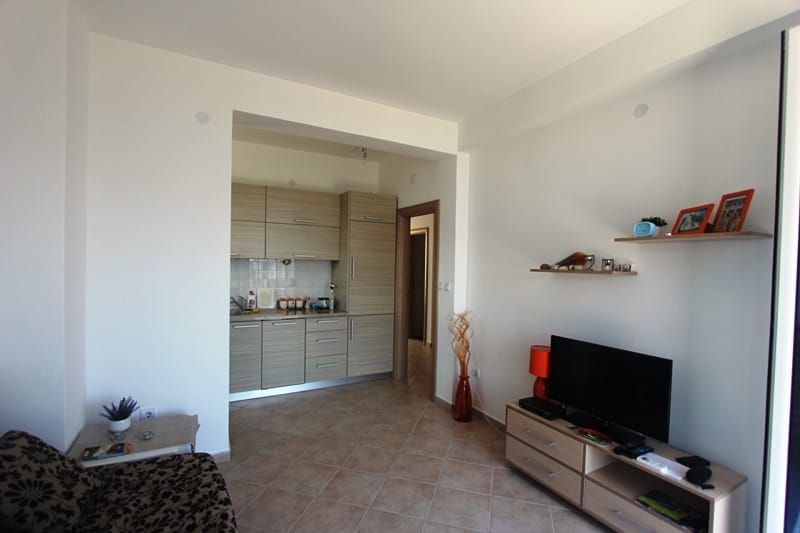 Living room with kitchen in a house in Baošići, Montenegro: bright interior, modern furniture, TV area, and tiled floor.