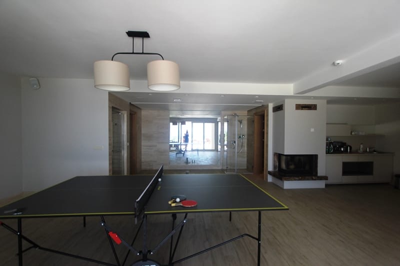 Living room with a tennis table, fireplace, and kitchen in a villa in Blizikuće, Montenegro. Modern interior with panoramic views.