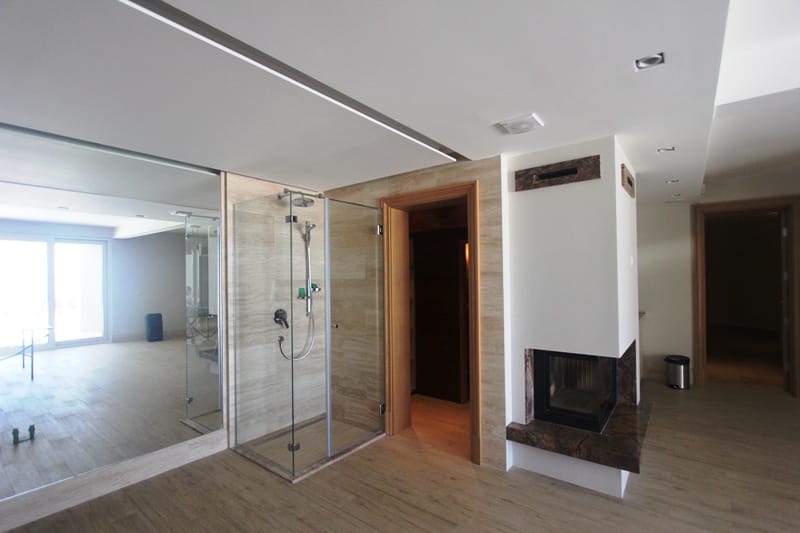Bathroom in a villa in Blizikuće, Montenegro: shower cabin, travertine finishes, and a modern fireplace in the interior.