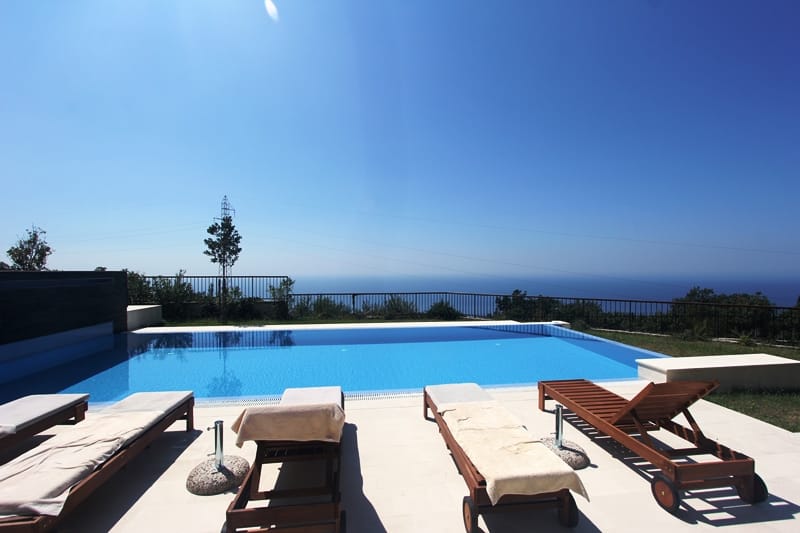 Outdoor pool with sea view at a villa in Blizikuće, Montenegro, with wooden sun loungers on the terrace.