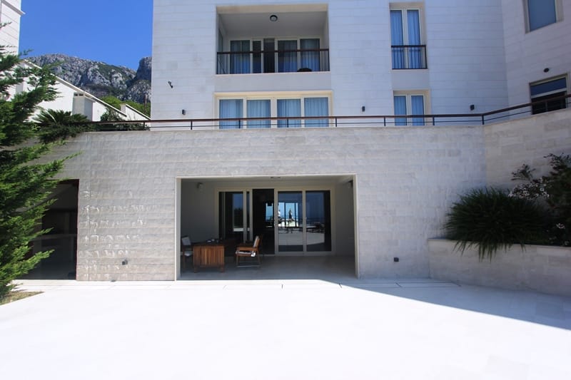 Facade of a modern villa in Blizikuće, Montenegro: stone cladding, a terrace with furniture, and panoramic sea views.