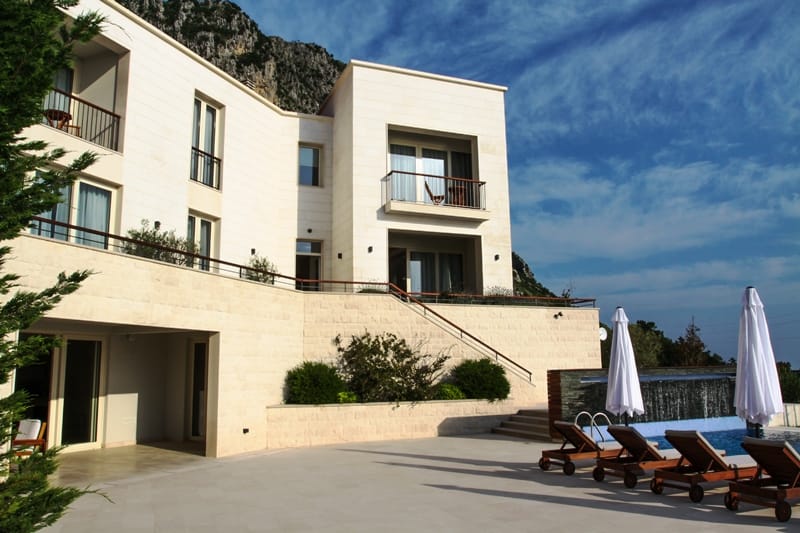 Modern villa in Blizikuće, Montenegro: stone facade, terrace with pool, sun loungers, and mountain views.