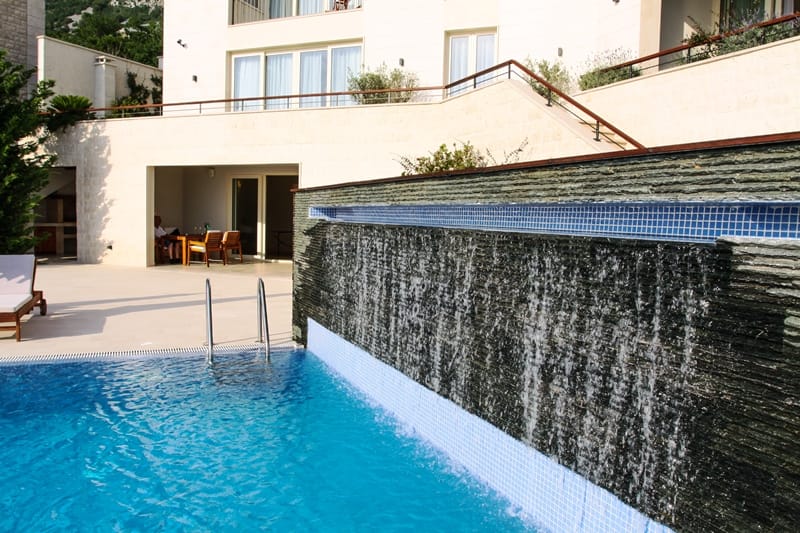 Pool with waterfall and terrace at a villa in Blizikuće, Montenegro: modern stone finish and a relaxation area by the water.