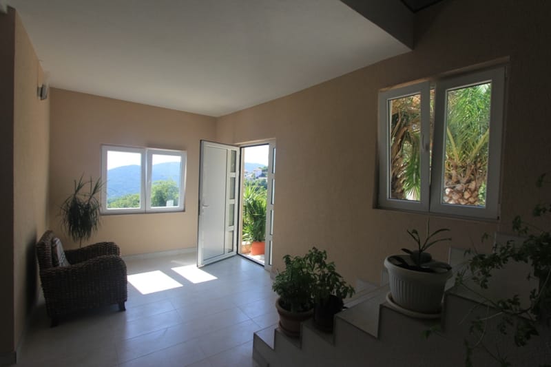 Bright living room in a house in Seoca, Montenegro: wicker chairs, panoramic windows with mountain views, and access to the terrace.