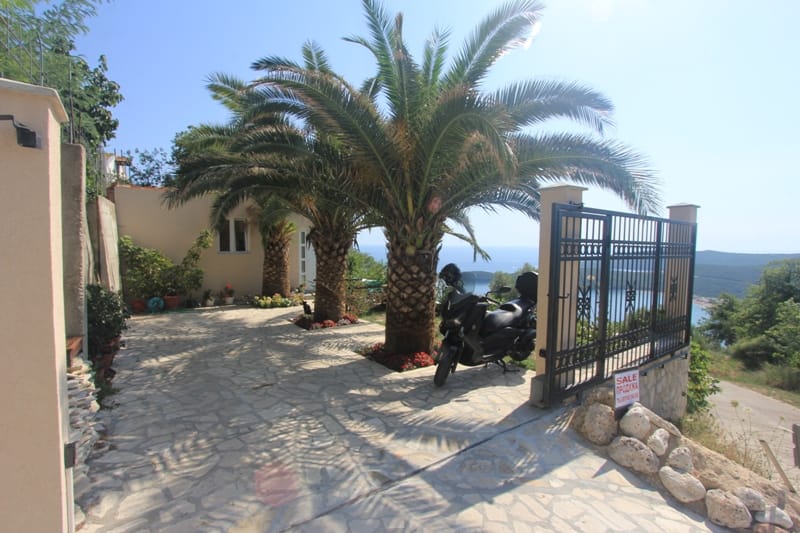 House courtyard in Seoce, Montenegro: paved area, palm trees, wrought-iron gates, and a panoramic sea view from the property.
