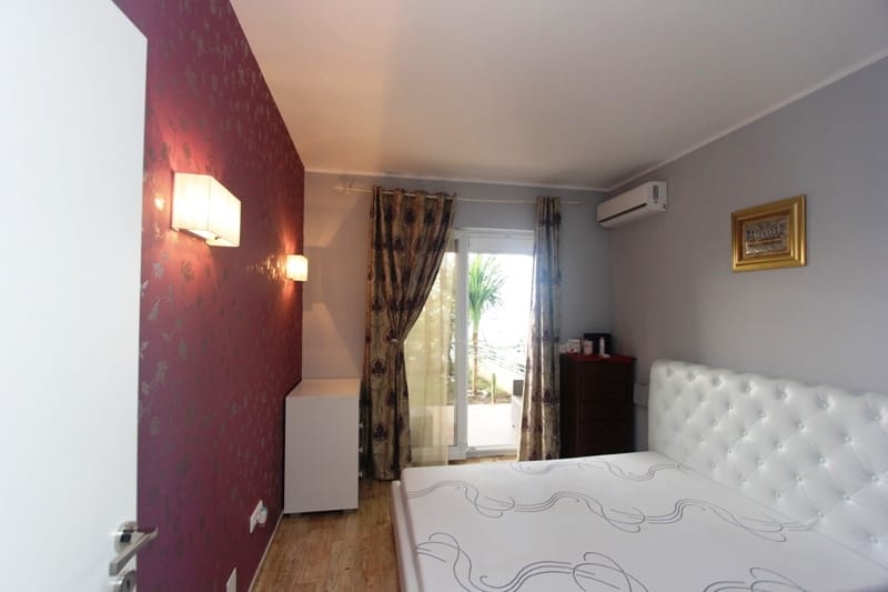 Bedroom with a white bed, an accent burgundy wall, and access to the terrace in a house, Uteha, Montenegro.