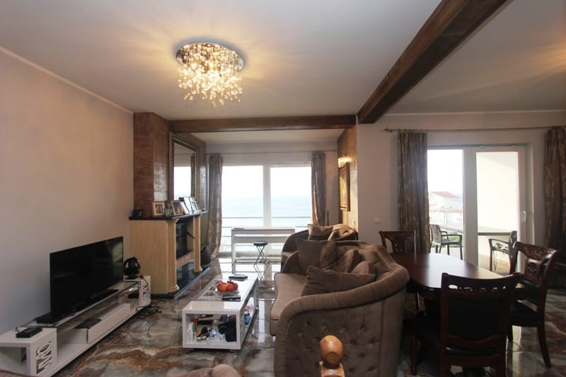 Living room with a fireplace and sea view in a house, Uteha, Montenegro: soft seating, dining area, and panoramic windows.
