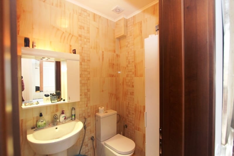 Bathroom in a house in Utjeha, Montenegro: beige tiles, sink, illuminated mirror, and plumbing fixtures.