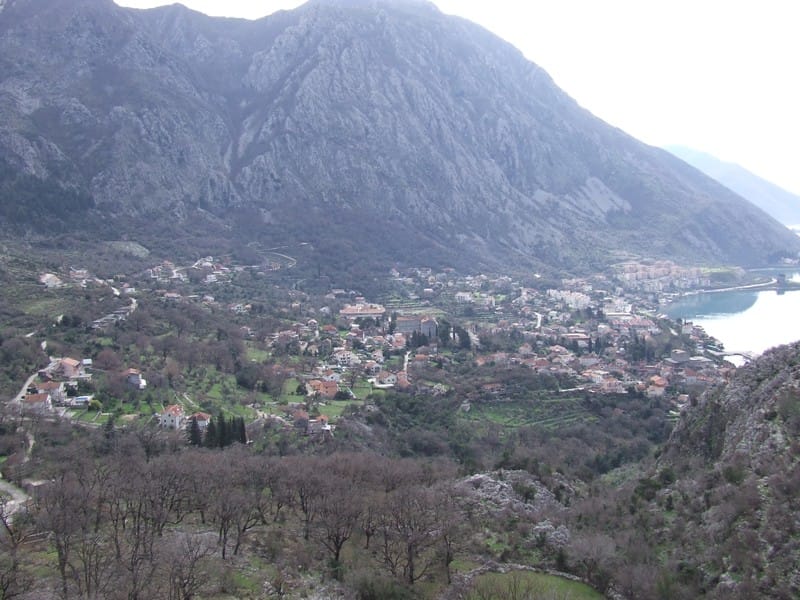 Panoramic view of the city of Risan and the Bay of Kotor in Montenegro from a plot of land surrounded by mountains and greenery.