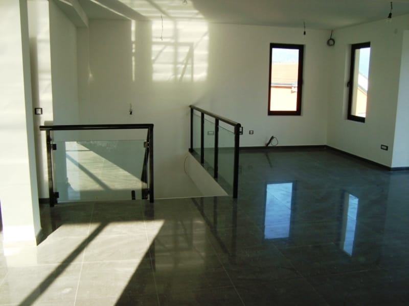 Spacious living room in Baošići, Montenegro: light finishes, glossy porcelain tile, and a staircase with glass railing.