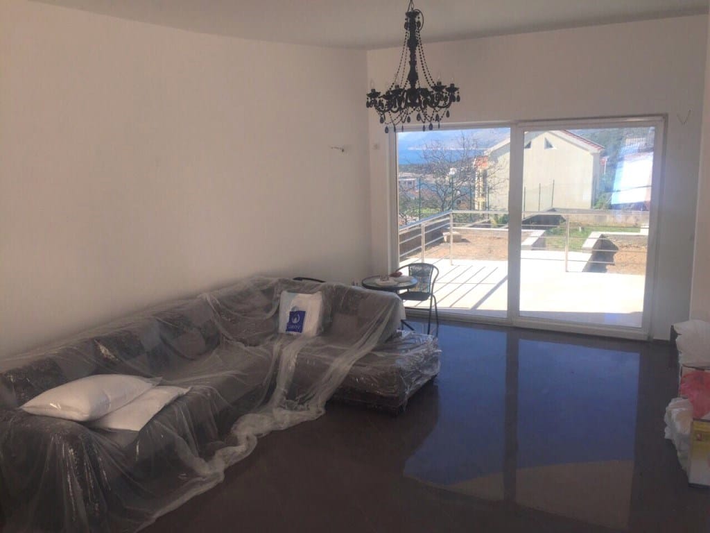 Living room in a villa in Utjeha, Montenegro: corner sofa, panoramic windows, terrace with sea view, and a stylish chandelier.