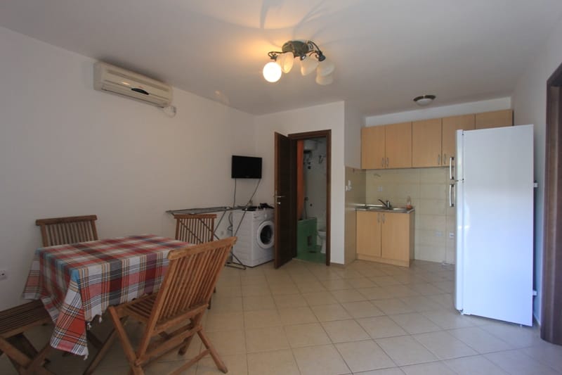 Living room with kitchen in a villa in Lepetane, Montenegro: dining area, light-colored furniture, appliances, and bathroom.