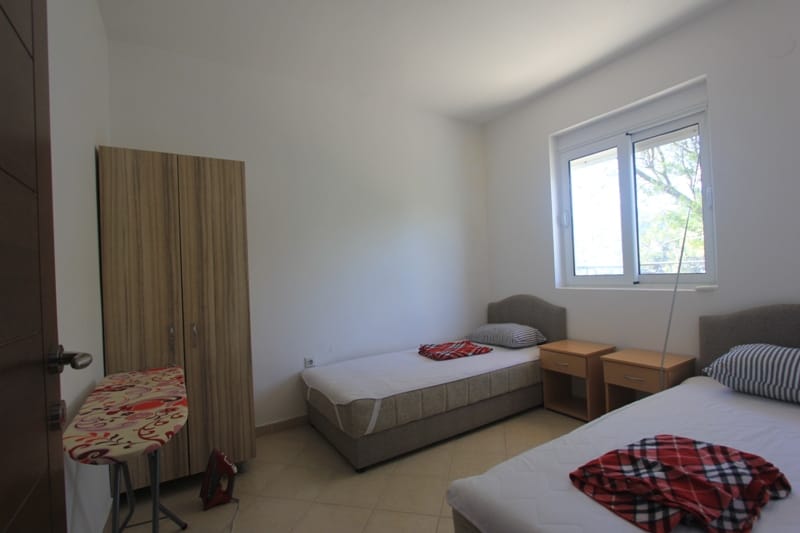 Bright bedroom with two beds, a wardrobe, and a window in a villa in Lepetane, Montenegro. Cozy furnished room.