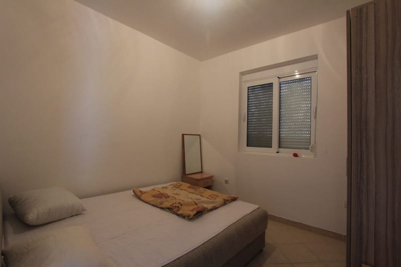 Bright bedroom with a double bed and wardrobe in a villa in Lepetani, Montenegro, with a window and security shutters.