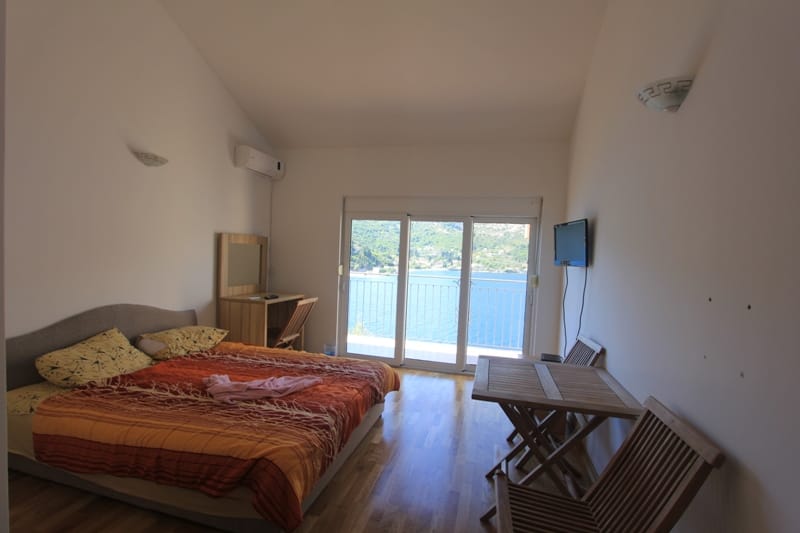 Bedroom in a villa in Lepetani, Montenegro: double bed, wooden furniture, and a panoramic sea view from the window.