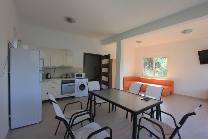 Living room with kitchen in a villa in Lepetani, Montenegro: dining area, light furniture, orange sofa, and appliances.
