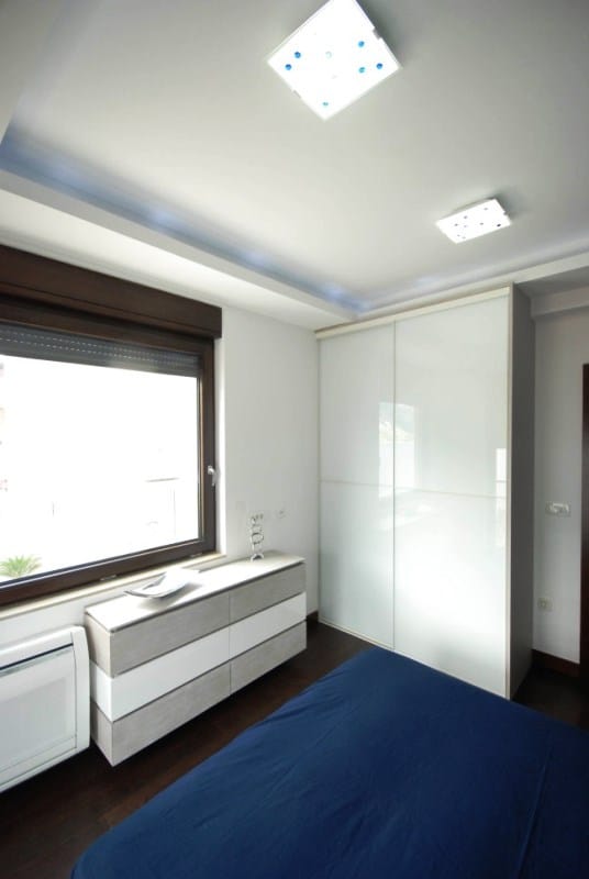 Modern bedroom with a white sliding wardrobe and dresser in a residential complex, Kostanica, Montenegro.