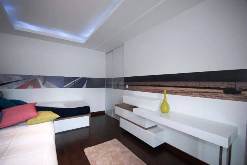 Modern bedroom in Kostanica residential complex, Montenegro: white furniture, dark flooring, ceiling lighting, and nautical wall decor.