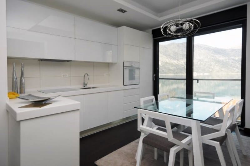 Modern white kitchen in Kostanica residential complex, Montenegro: dining area, panoramic view of the sea and mountains from the window.