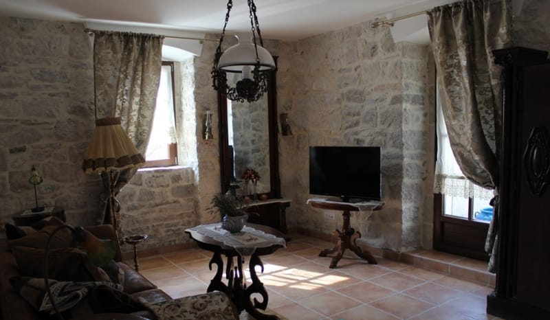 Living room in a stone house in Strp, Montenegro: vintage furniture, natural stone walls, and tiled flooring.