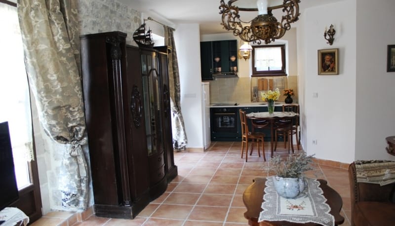 Living room with kitchen in a house in Strp, Montenegro: stone wall, antique cabinet, tiled floor, and cozy furniture.
