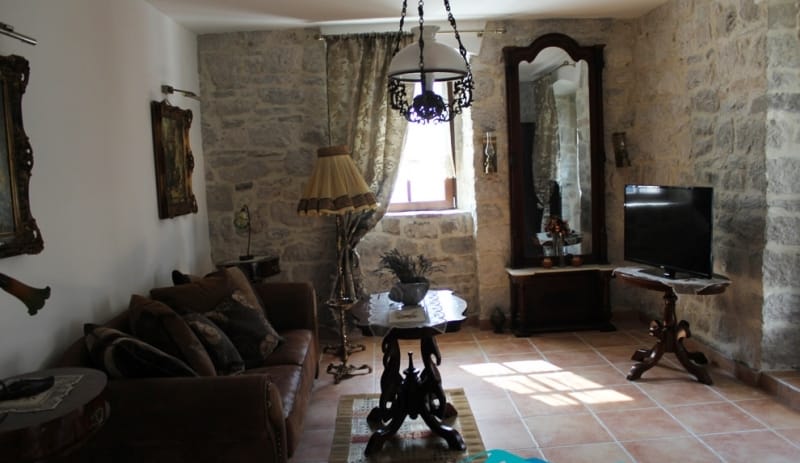 Living room in a stone house in Strp, Montenegro: vintage furniture, natural stone walls, and tiled flooring.