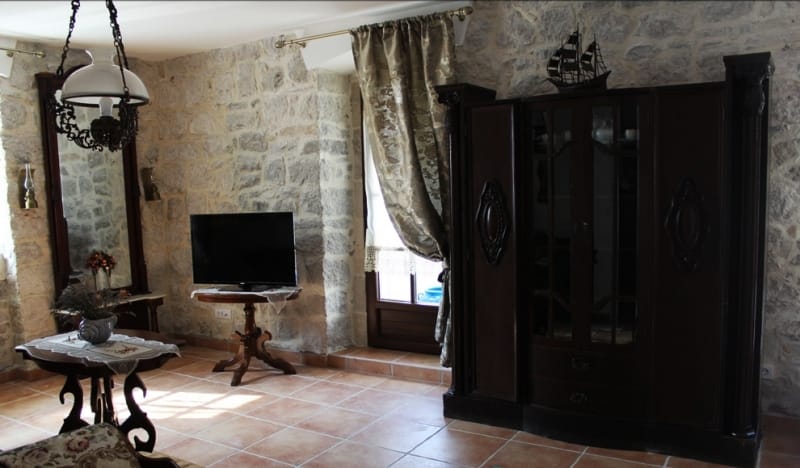 Living room in a stone house in Strp, Montenegro: antique furniture, natural stone walls, and tiled flooring.